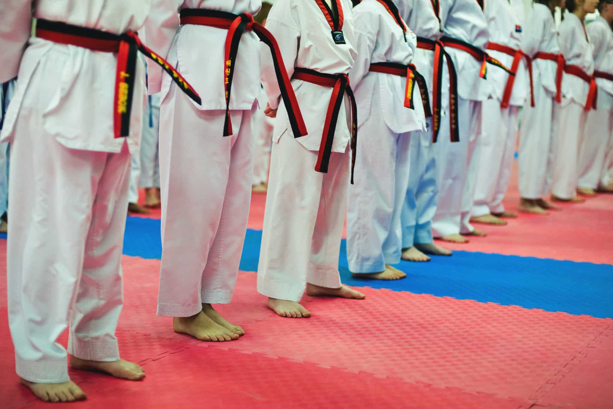 Midwest Tae Kwon Do kids in white gi stand in a line on the mat from the waist down.