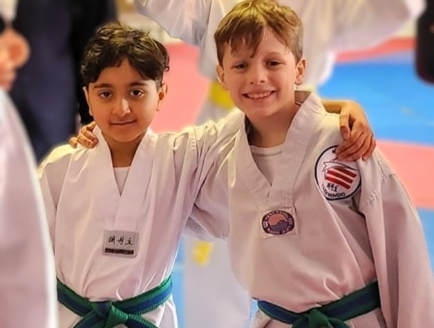 Midwest Tae Kwon Do kids in gi smiling at camera with their arms around each others shoulders.